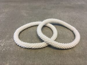 Roll-on armbånd som passer til næsten alle kvinder. Kvindegrupper i Nepal, Kathmandu Valley, udstyres med glasperler og bomuldsgarn, så de i deres fritid kan hækler disse smukke perlearmbånd. Den ekstra indtægt går bl.a. til at sende kvindernes børn i skole. Hvert armbånd er et unikt resultat af kvindernes håndarbejde og varierer i farvekombinationer og mønstre.
