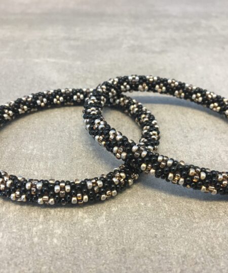 Roll-on armbånd som passer til næsten alle kvinder. Kvindegrupper i Nepal, Kathmandu Valley, udstyres med glasperler og bomuldsgarn, så de i deres fritid kan hækler disse smukke perlearmbånd. Den ekstra indtægt går bl.a. til at sende kvindernes børn i skole. Hvert armbånd er et unikt resultat af kvindernes håndarbejde og varierer i farvekombinationer og mønstre.