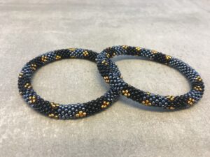 Roll-on armbånd som passer til næsten alle kvinder. Kvindegrupper i Nepal, Kathmandu Valley, udstyres med glasperler og bomuldsgarn, så de i deres fritid kan hækler disse smukke perlearmbånd. Den ekstra indtægt går bl.a. til at sende kvindernes børn i skole. Hvert armbånd er et unikt resultat af kvindernes håndarbejde og varierer i farvekombinationer og mønstre.