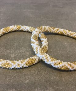 Roll-on armbånd som passer til næsten alle kvinder. Kvindegrupper i Nepal, Kathmandu Valley, udstyres med glasperler og bomuldsgarn, så de i deres fritid kan hækler disse smukke perlearmbånd. Den ekstra indtægt går bl.a. til at sende kvindernes børn i skole. Hvert armbånd er et unikt resultat af kvindernes håndarbejde og varierer i farvekombinationer og mønstre.