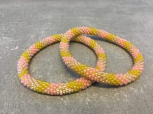 Roll-on armbånd som passer til næsten alle kvinder. Kvindegrupper i Nepal, Kathmandu Valley, udstyres med glasperler og bomuldsgarn, så de i deres fritid kan hækler disse smukke perlearmbånd. Den ekstra indtægt går bl.a. til at sende kvindernes børn i skole. Hvert armbånd er et unikt resultat af kvindernes håndarbejde og varierer i farvekombinationer og mønstre.