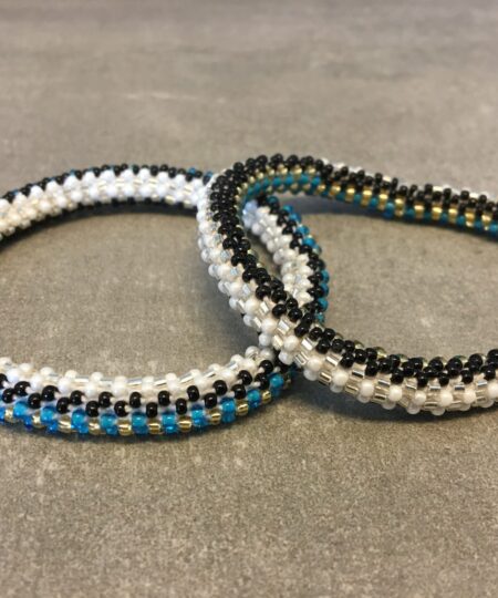 Roll-on armbånd som passer til næsten alle kvinder. Kvindegrupper i Nepal, Kathmandu Valley, udstyres med glasperler og bomuldsgarn, så de i deres fritid kan hækler disse smukke perlearmbånd. Den ekstra indtægt går bl.a. til at sende kvindernes børn i skole. Hvert armbånd er et unikt resultat af kvindernes håndarbejde og varierer i farvekombinationer og mønstre.