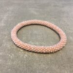 Roll-on armbånd som passer til næsten alle kvinder. Kvindegrupper i Nepal, Kathmandu Valley, udstyres med glasperler og bomuldsgarn, så de i deres fritid kan hækler disse smukke perlearmbånd. Den ekstra indtægt går bl.a. til at sende kvindernes børn i skole. Hvert armbånd er et unikt resultat af kvindernes håndarbejde og varierer i farvekombinationer og mønstre.