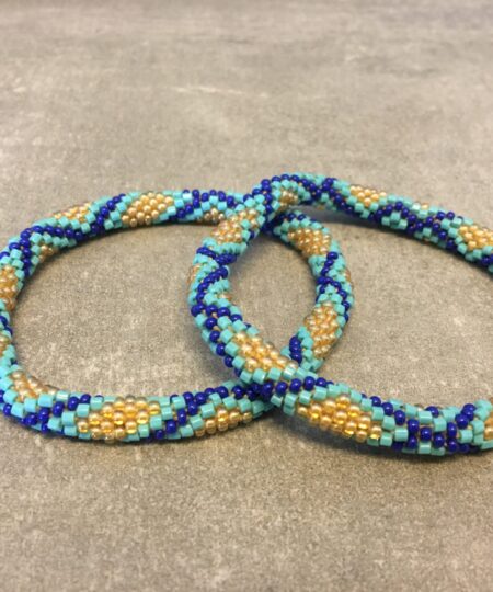 Roll-on armbånd som passer til næsten alle kvinder. Kvindegrupper i Nepal, Kathmandu Valley, udstyres med glasperler og bomuldsgarn, så de i deres fritid kan hækler disse smukke perlearmbånd. Den ekstra indtægt går bl.a. til at sende kvindernes børn i skole. Hvert armbånd er et unikt resultat af kvindernes håndarbejde og varierer i farvekombinationer og mønstre.