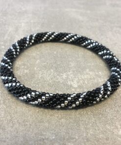 Roll-on armbånd som passer til næsten alle kvinder. Kvindegrupper i Nepal, Kathmandu Valley, udstyres med glasperler og bomuldsgarn, så de i deres fritid kan hækler disse smukke perlearmbånd. Den ekstra indtægt går bl.a. til at sende kvindernes børn i skole. Hvert armbånd er et unikt resultat af kvindernes håndarbejde og varierer i farvekombinationer og mønstre.