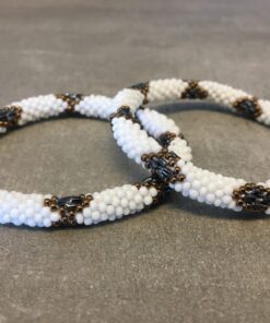 Roll-on armbånd som passer til næsten alle kvinder. Kvindegrupper i Nepal, Kathmandu Valley, udstyres med glasperler og bomuldsgarn, så de i deres fritid kan hækler disse smukke perlearmbånd. Den ekstra indtægt går bl.a. til at sende kvindernes børn i skole. Hvert armbånd er et unikt resultat af kvindernes håndarbejde og varierer i farvekombinationer og mønstre.