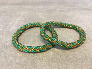 Roll-on armbånd som passer til næsten alle kvinder. Kvindegrupper i Nepal, Kathmandu Valley, udstyres med glasperler og bomuldsgarn, så de i deres fritid kan hækler disse smukke perlearmbånd. Den ekstra indtægt går bl.a. til at sende kvindernes børn i skole. Hvert armbånd er et unikt resultat af kvindernes håndarbejde og varierer i farvekombinationer og mønstre.