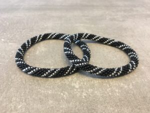 Roll-on armbånd som passer til næsten alle kvinder. Kvindegrupper i Nepal, Kathmandu Valley, udstyres med glasperler og bomuldsgarn, så de i deres fritid kan hækler disse smukke perlearmbånd. Den ekstra indtægt går bl.a. til at sende kvindernes børn i skole. Hvert armbånd er et unikt resultat af kvindernes håndarbejde og varierer i farvekombinationer og mønstre.