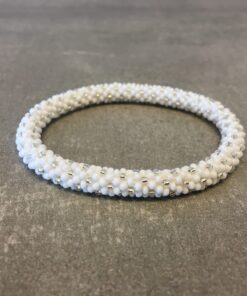 Roll-on armbånd som passer til næsten alle kvinder. Kvindegrupper i Nepal, Kathmandu Valley, udstyres med glasperler og bomuldsgarn, så de i deres fritid kan hækler disse smukke perlearmbånd. Den ekstra indtægt går bl.a. til at sende kvindernes børn i skole. Hvert armbånd er et unikt resultat af kvindernes håndarbejde og varierer i farvekombinationer og mønstre.