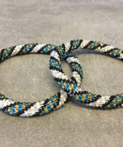 Roll-on armbånd som passer til næsten alle kvinder. Kvindegrupper i Nepal, Kathmandu Valley, udstyres med glasperler og bomuldsgarn, så de i deres fritid kan hækler disse smukke perlearmbånd. Den ekstra indtægt går bl.a. til at sende kvindernes børn i skole. Hvert armbånd er et unikt resultat af kvindernes håndarbejde og varierer i farvekombinationer og mønstre.