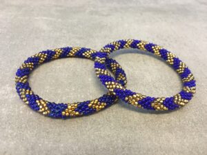 Roll-on armbånd som passer til næsten alle kvinder. Kvindegrupper i Nepal, Kathmandu Valley, udstyres med glasperler og bomuldsgarn, så de i deres fritid kan hækler disse smukke perlearmbånd. Den ekstra indtægt går bl.a. til at sende kvindernes børn i skole. Hvert armbånd er et unikt resultat af kvindernes håndarbejde og varierer i farvekombinationer og mønstre.