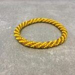Roll-on armbånd som passer til næsten alle kvinder. Kvindegrupper i Nepal, Kathmandu Valley, udstyres med glasperler og bomuldsgarn, så de i deres fritid kan hækler disse smukke perlearmbånd. Den ekstra indtægt går bl.a. til at sende kvindernes børn i skole. Hvert armbånd er et unikt resultat af kvindernes håndarbejde og varierer i farvekombinationer og mønstre.