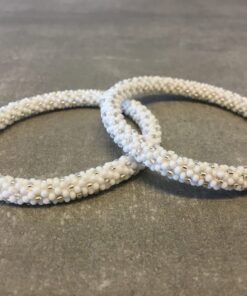 Roll-on armbånd som passer til næsten alle kvinder. Kvindegrupper i Nepal, Kathmandu Valley, udstyres med glasperler og bomuldsgarn, så de i deres fritid kan hækler disse smukke perlearmbånd. Den ekstra indtægt går bl.a. til at sende kvindernes børn i skole. Hvert armbånd er et unikt resultat af kvindernes håndarbejde og varierer i farvekombinationer og mønstre.