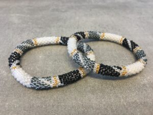 Roll-on armbånd som passer til næsten alle kvinder. Kvindegrupper i Nepal, Kathmandu Valley, udstyres med glasperler og bomuldsgarn, så de i deres fritid kan hækler disse smukke perlearmbånd. Den ekstra indtægt går bl.a. til at sende kvindernes børn i skole. Hvert armbånd er et unikt resultat af kvindernes håndarbejde og varierer i farvekombinationer og mønstre.