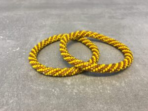 Roll-on armbånd som passer til næsten alle kvinder. Kvindegrupper i Nepal, Kathmandu Valley, udstyres med glasperler og bomuldsgarn, så de i deres fritid kan hækler disse smukke perlearmbånd. Den ekstra indtægt går bl.a. til at sende kvindernes børn i skole. Hvert armbånd er et unikt resultat af kvindernes håndarbejde og varierer i farvekombinationer og mønstre.