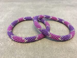 Roll-on armbånd som passer til næsten alle kvinder. Kvindegrupper i Nepal, Kathmandu Valley, udstyres med glasperler og bomuldsgarn, så de i deres fritid kan hækler disse smukke perlearmbånd. Den ekstra indtægt går bl.a. til at sende kvindernes børn i skole. Hvert armbånd er et unikt resultat af kvindernes håndarbejde og varierer i farvekombinationer og mønstre.