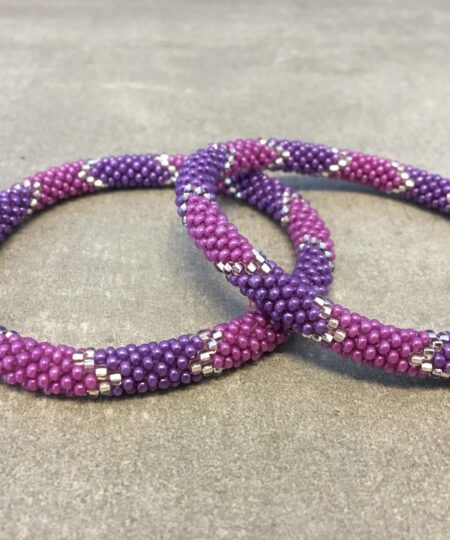 Roll-on armbånd som passer til næsten alle kvinder. Kvindegrupper i Nepal, Kathmandu Valley, udstyres med glasperler og bomuldsgarn, så de i deres fritid kan hækler disse smukke perlearmbånd. Den ekstra indtægt går bl.a. til at sende kvindernes børn i skole. Hvert armbånd er et unikt resultat af kvindernes håndarbejde og varierer i farvekombinationer og mønstre.