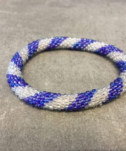 Roll-on armbånd som passer til næsten alle kvinder. Kvindegrupper i Nepal, Kathmandu Valley, udstyres med glasperler og bomuldsgarn, så de i deres fritid kan hækler disse smukke perlearmbånd. Den ekstra indtægt går bl.a. til at sende kvindernes børn i skole. Hvert armbånd er et unikt resultat af kvindernes håndarbejde og varierer i farvekombinationer og mønstre.