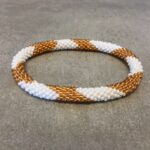 Roll-on armbånd som passer til næsten alle kvinder. Kvindegrupper i Nepal, Kathmandu Valley, udstyres med glasperler og bomuldsgarn, så de i deres fritid kan hækler disse smukke perlearmbånd. Den ekstra indtægt går bl.a. til at sende kvindernes børn i skole. Hvert armbånd er et unikt resultat af kvindernes håndarbejde og varierer i farvekombinationer og mønstre.