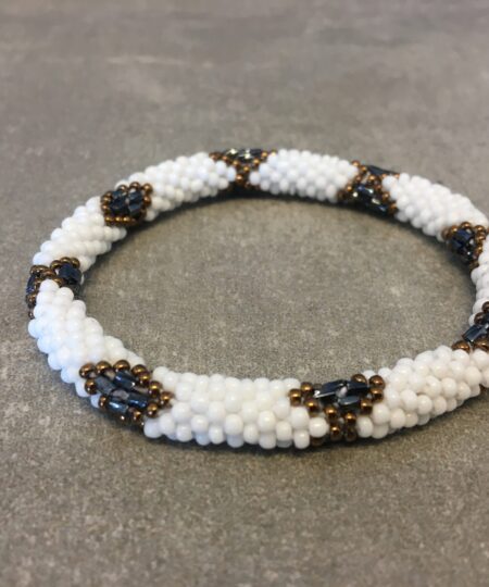 Roll-on armbånd som passer til næsten alle kvinder. Kvindegrupper i Nepal, Kathmandu Valley, udstyres med glasperler og bomuldsgarn, så de i deres fritid kan hækler disse smukke perlearmbånd. Den ekstra indtægt går bl.a. til at sende kvindernes børn i skole. Hvert armbånd er et unikt resultat af kvindernes håndarbejde og varierer i farvekombinationer og mønstre.