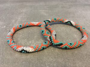 Roll-on armbånd som passer til næsten alle kvinder. Kvindegrupper i Nepal, Kathmandu Valley, udstyres med glasperler og bomuldsgarn, så de i deres fritid kan hækler disse smukke perlearmbånd. Den ekstra indtægt går bl.a. til at sende kvindernes børn i skole. Hvert armbånd er et unikt resultat af kvindernes håndarbejde og varierer i farvekombinationer og mønstre.