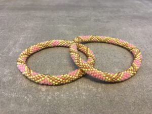 Roll-on armbånd som passer til næsten alle kvinder. Kvindegrupper i Nepal, Kathmandu Valley, udstyres med glasperler og bomuldsgarn, så de i deres fritid kan hækler disse smukke perlearmbånd. Den ekstra indtægt går bl.a. til at sende kvindernes børn i skole. Hvert armbånd er et unikt resultat af kvindernes håndarbejde og varierer i farvekombinationer og mønstre.