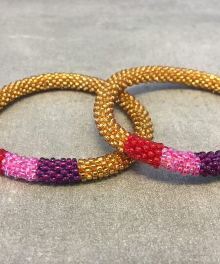 Roll-on armbånd som passer til næsten alle kvinder. Kvindegrupper i Nepal, Kathmandu Valley, udstyres med glasperler og bomuldsgarn, så de i deres fritid kan hækler disse smukke perlearmbånd. Den ekstra indtægt går bl.a. til at sende kvindernes børn i skole. Hvert armbånd er et unikt resultat af kvindernes håndarbejde og varierer i farvekombinationer og mønstre.