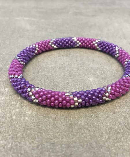 Roll-on armbånd som passer til næsten alle kvinder. Kvindegrupper i Nepal, Kathmandu Valley, udstyres med glasperler og bomuldsgarn, så de i deres fritid kan hækler disse smukke perlearmbånd. Den ekstra indtægt går bl.a. til at sende kvindernes børn i skole. Hvert armbånd er et unikt resultat af kvindernes håndarbejde og varierer i farvekombinationer og mønstre.