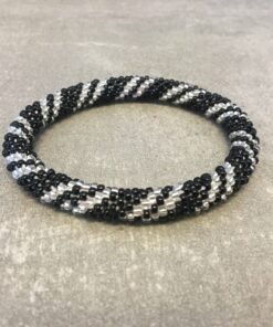 Roll-on armbånd som passer til næsten alle kvinder. Kvindegrupper i Nepal, Kathmandu Valley, udstyres med glasperler og bomuldsgarn, så de i deres fritid kan hækler disse smukke perlearmbånd. Den ekstra indtægt går bl.a. til at sende kvindernes børn i skole. Hvert armbånd er et unikt resultat af kvindernes håndarbejde og varierer i farvekombinationer og mønstre.