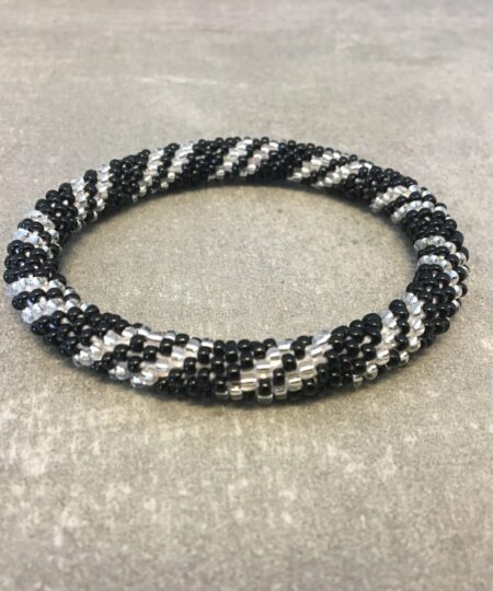 Roll-on armbånd som passer til næsten alle kvinder. Kvindegrupper i Nepal, Kathmandu Valley, udstyres med glasperler og bomuldsgarn, så de i deres fritid kan hækler disse smukke perlearmbånd. Den ekstra indtægt går bl.a. til at sende kvindernes børn i skole. Hvert armbånd er et unikt resultat af kvindernes håndarbejde og varierer i farvekombinationer og mønstre.