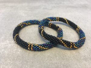 Roll-on armbånd som passer til næsten alle kvinder. Kvindegrupper i Nepal, Kathmandu Valley, udstyres med glasperler og bomuldsgarn, så de i deres fritid kan hækler disse smukke perlearmbånd. Den ekstra indtægt går bl.a. til at sende kvindernes børn i skole. Hvert armbånd er et unikt resultat af kvindernes håndarbejde og varierer i farvekombinationer og mønstre.