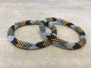 Roll-on armbånd som passer til næsten alle kvinder. Kvindegrupper i Nepal, Kathmandu Valley, udstyres med glasperler og bomuldsgarn, så de i deres fritid kan hækler disse smukke perlearmbånd. Den ekstra indtægt går bl.a. til at sende kvindernes børn i skole. Hvert armbånd er et unikt resultat af kvindernes håndarbejde og varierer i farvekombinationer og mønstre.