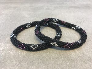 Roll-on armbånd som passer til næsten alle kvinder. Kvindegrupper i Nepal, Kathmandu Valley, udstyres med glasperler og bomuldsgarn, så de i deres fritid kan hækler disse smukke perlearmbånd. Den ekstra indtægt går bl.a. til at sende kvindernes børn i skole. Hvert armbånd er et unikt resultat af kvindernes håndarbejde og varierer i farvekombinationer og mønstre.