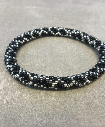 Roll-on armbånd som passer til næsten alle kvinder. Kvindegrupper i Nepal, Kathmandu Valley, udstyres med glasperler og bomuldsgarn, så de i deres fritid kan hækler disse smukke perlearmbånd. Den ekstra indtægt går bl.a. til at sende kvindernes børn i skole. Hvert armbånd er et unikt resultat af kvindernes håndarbejde og varierer i farvekombinationer og mønstre.