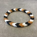 Roll-on armbånd som passer til næsten alle kvinder. Kvindegrupper i Nepal, Kathmandu Valley, udstyres med glasperler og bomuldsgarn, så de i deres fritid kan hækler disse smukke perlearmbånd. Den ekstra indtægt går bl.a. til at sende kvindernes børn i skole. Hvert armbånd er et unikt resultat af kvindernes håndarbejde og varierer i farvekombinationer og mønstre.