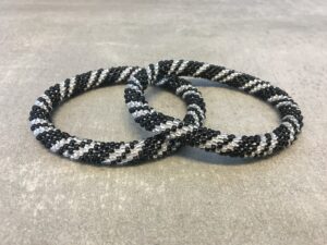 Roll-on armbånd som passer til næsten alle kvinder. Kvindegrupper i Nepal, Kathmandu Valley, udstyres med glasperler og bomuldsgarn, så de i deres fritid kan hækler disse smukke perlearmbånd. Den ekstra indtægt går bl.a. til at sende kvindernes børn i skole. Hvert armbånd er et unikt resultat af kvindernes håndarbejde og varierer i farvekombinationer og mønstre.