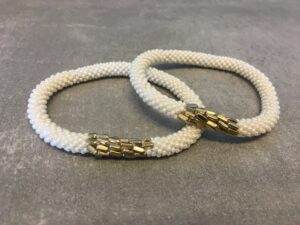 Roll-on armbånd som passer til næsten alle kvinder. Kvindegrupper i Nepal, Kathmandu Valley, udstyres med glasperler og bomuldsgarn, så de i deres fritid kan hækler disse smukke perlearmbånd. Den ekstra indtægt går bl.a. til at sende kvindernes børn i skole. Hvert armbånd er et unikt resultat af kvindernes håndarbejde og varierer i farvekombinationer og mønstre.