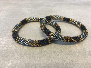 Roll-on armbånd som passer til næsten alle kvinder. Kvindegrupper i Nepal, Kathmandu Valley, udstyres med glasperler og bomuldsgarn, så de i deres fritid kan hækler disse smukke perlearmbånd. Den ekstra indtægt går bl.a. til at sende kvindernes børn i skole. Hvert armbånd er et unikt resultat af kvindernes håndarbejde og varierer i farvekombinationer og mønstre.