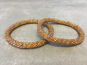 Roll-on armbånd som passer til næsten alle kvinder. Kvindegrupper i Nepal, Kathmandu Valley, udstyres med glasperler og bomuldsgarn, så de i deres fritid kan hækler disse smukke perlearmbånd. Den ekstra indtægt går bl.a. til at sende kvindernes børn i skole. Hvert armbånd er et unikt resultat af kvindernes håndarbejde og varierer i farvekombinationer og mønstre.