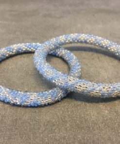 Roll-on armbånd som passer til næsten alle kvinder. Kvindegrupper i Nepal, Kathmandu Valley, udstyres med glasperler og bomuldsgarn, så de i deres fritid kan hækler disse smukke perlearmbånd. Den ekstra indtægt går bl.a. til at sende kvindernes børn i skole. Hvert armbånd er et unikt resultat af kvindernes håndarbejde og varierer i farvekombinationer og mønstre.