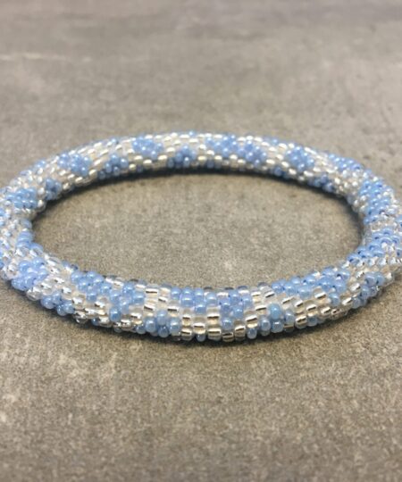 Roll-on armbånd som passer til næsten alle kvinder. Kvindegrupper i Nepal, Kathmandu Valley, udstyres med glasperler og bomuldsgarn, så de i deres fritid kan hækler disse smukke perlearmbånd. Den ekstra indtægt går bl.a. til at sende kvindernes børn i skole. Hvert armbånd er et unikt resultat af kvindernes håndarbejde og varierer i farvekombinationer og mønstre.