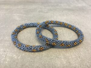 Roll-on armbånd som passer til næsten alle kvinder. Kvindegrupper i Nepal, Kathmandu Valley, udstyres med glasperler og bomuldsgarn, så de i deres fritid kan hækler disse smukke perlearmbånd. Den ekstra indtægt går bl.a. til at sende kvindernes børn i skole. Hvert armbånd er et unikt resultat af kvindernes håndarbejde og varierer i farvekombinationer og mønstre.