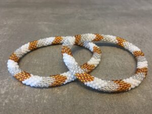 Roll-on armbånd som passer til næsten alle kvinder. Kvindegrupper i Nepal, Kathmandu Valley, udstyres med glasperler og bomuldsgarn, så de i deres fritid kan hækler disse smukke perlearmbånd. Den ekstra indtægt går bl.a. til at sende kvindernes børn i skole. Hvert armbånd er et unikt resultat af kvindernes håndarbejde og varierer i farvekombinationer og mønstre.