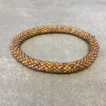 Roll-on armbånd som passer til næsten alle kvinder. Kvindegrupper i Nepal, Kathmandu Valley, udstyres med glasperler og bomuldsgarn, så de i deres fritid kan hækler disse smukke perlearmbånd. Den ekstra indtægt går bl.a. til at sende kvindernes børn i skole. Hvert armbånd er et unikt resultat af kvindernes håndarbejde og varierer i farvekombinationer og mønstre.