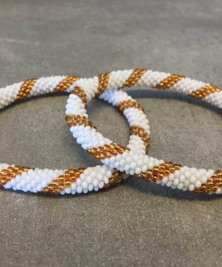 Roll-on armbånd som passer til næsten alle kvinder. Kvindegrupper i Nepal, Kathmandu Valley, udstyres med glasperler og bomuldsgarn, så de i deres fritid kan hækler disse smukke perlearmbånd. Den ekstra indtægt går bl.a. til at sende kvindernes børn i skole. Hvert armbånd er et unikt resultat af kvindernes håndarbejde og varierer i farvekombinationer og mønstre.