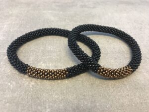 Roll-on armbånd som passer til næsten alle kvinder. Kvindegrupper i Nepal, Kathmandu Valley, udstyres med glasperler og bomuldsgarn, så de i deres fritid kan hækler disse smukke perlearmbånd. Den ekstra indtægt går bl.a. til at sende kvindernes børn i skole. Hvert armbånd er et unikt resultat af kvindernes håndarbejde og varierer i farvekombinationer og mønstre.
