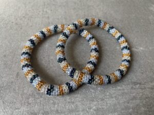 Nepal armbånd er en inspirerende og fascinerende smykkegenre, der vækker interessen hos smykkeentusiaster over hele verden. Disse håndlavede armbånd er kunstværker, der udstråler autenticitet, skønhed og dyb symbolik. Lad os dykke ned i den betagende verden af Nepal armbånd og udforske, hvad der gør dem så unikke og eftertragtede. Hvert Nepal armbånd er unikt, og det er netop denne individualitet, der appellerer til mange. Armbåndene er ofte skabt af dygtige nepalesiske håndværkere, der gennem generationer har forfinet deres teknikker til at skabe smykker af høj kvalitet. Disse håndværkere bruger traditionelle metoder, som har været en del af Nepals kultur og historie i århundreder. Processen er omhyggelig og kræver en stor grad af præcision og tålmodighed, hvilket gør hvert armbånd til en kærlighedsfyldt skabelse. Nepal armbånd er kendt for deres farverige og levende design. De er ofte dekoreret med perler, ædelstene, træ, metal eller andre naturlige materialer, hvilket giver dem et unikt udseende. Hvert enkelt element, der anvendes i armbåndene, er udvalgt omhyggeligt for at skabe en harmonisk kombination af farver og teksturer. Disse elementer er ofte inspireret af Nepals rige natur og kultur, hvilket giver armbåndene en autentisk følelse og en stærk forbindelse til landet. Symbolik spiller også en vigtig rolle i Nepal armbåndenes popularitet. Mange af armbåndene har indgraverede mønstre eller symboler, der repræsenterer vigtige aspekter af Nepals traditioner og spiritualitet. Disse symboler kan have betydning for held, lykke, kærlighed, beskyttelse eller en dybere forbindelse til naturen. At bære et Nepal armbånd kan derfor have en dybere betydning for bæreren og kan fungere som en påmindelse om deres forbindelse til Nepals rige arv. Nepal armbånd er ikke kun smukke smykker, men de har også en stærk social og kulturel betydning. Mange af disse smykker er håndlavede af kvinder, der er en del af samfundet i landområderne i Nepal. Produktionen af armbåndene giver disse kvinder mulighed for at skabe en bæredygtig indkomst, forbedre deres levevilkår og styrke deres selvstændighed. Når du køber et Nepal armbånd, bidrager du derfor til at støtte en positiv social indvirkning og bevare traditionelle håndværksmæssige metoder. Udover deres kulturelle og sociale betydning er Nepal armbånd også en favorit blandt modebevidste enkeltpersoner, der ønsker at tilføje en unik og autentisk touch til deres stil. Disse armbånd kan styles på utallige måder, uanset om du ønsker at skabe et bohemeinspireret look, en farverig festlig stil eller en subtil og elegant kombination. Der er et Nepal armbånd til enhver lejlighed og enhver personlig præference. I det store udvalg af smykker, der findes i dagens marked, skiller Nepal armbånd sig ud som en særlig perle. Deres håndlavede karakter, farverige design, dybe symbolik og sociale indvirkning gør dem til mere end bare smykker - de er en form for kunst og kultur, der fortæller historien om Nepal og dets folk. Ved at bære et Nepal armbånd, bærer du også med dig en del af dette rige og inspirerende land. Så uanset om du leder efter en meningsfuld gave eller ønsker at berige din egen smykkesamling, vil et Nepal armbånd være et mindeværdigt og værdsat valg.