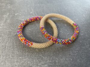 Unikke håndlavet nepal armbånd af glasperler- Som er knyttet perle for perle – Af Nepalesiske Kvinder.  Kvindegrupper i Nepal, Kathmandu Valley, udstyres med glasperler og bomuldsgarn, så de i deres fritid kan håndknytte de smukke perlearmbånd. Hvert armbånd er et unikt resultat af kvindernes håndarbejde og varierer i farvekombinationer og mønstre. De er hæklet med en bomuldssnor. Syntes man at de lidt stramme, kan man vride forsigtigt i dem så de bliver større. syntes man derimod at de er blive lidt for løse, kan man ligge dem i vand. dette gør at bomuldssnoren trækker sig sammen og de bliver mindre igen. Unikke håndlavet nepal armbånd, som er knyttet perle for perle, af nepalesiske kvinder. Vi har mere end 200 forskellige, at vælge i mellem. Så du kan finde de helt rigtige roll on nepal perle armbånd.