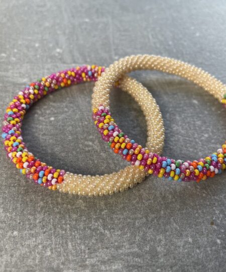 Unikke håndlavet nepal armbånd af glasperler- Som er knyttet perle for perle – Af Nepalesiske Kvinder.  Kvindegrupper i Nepal, Kathmandu Valley, udstyres med glasperler og bomuldsgarn, så de i deres fritid kan håndknytte de smukke perlearmbånd. Hvert armbånd er et unikt resultat af kvindernes håndarbejde og varierer i farvekombinationer og mønstre. De er hæklet med en bomuldssnor. Syntes man at de lidt stramme, kan man vride forsigtigt i dem så de bliver større. syntes man derimod at de er blive lidt for løse, kan man ligge dem i vand. dette gør at bomuldssnoren trækker sig sammen og de bliver mindre igen. Unikke håndlavet nepal armbånd, som er knyttet perle for perle, af nepalesiske kvinder. Vi har mere end 200 forskellige, at vælge i mellem. Så du kan finde de helt rigtige roll on nepal perle armbånd.