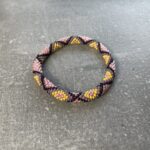 Unikke håndlavet nepal armbånd af glasperler- Som er knyttet perle for perle – Af Nepalesiske Kvinder.  Kvindegrupper i Nepal, Kathmandu Valley, udstyres med glasperler og bomuldsgarn, så de i deres fritid kan håndknytte de smukke perlearmbånd. Hvert armbånd er et unikt resultat af kvindernes håndarbejde og varierer i farvekombinationer og mønstre. De er hæklet med en bomuldssnor. Syntes man at de lidt stramme, kan man vride forsigtigt i dem så de bliver større. syntes man derimod at de er blive lidt for løse, kan man ligge dem i vand. dette gør at bomuldssnoren trækker sig sammen og de bliver mindre igen. Unikke håndlavet nepal armbånd, som er knyttet perle for perle, af nepalesiske kvinder. Vi har mere end 200 forskellige, at vælge i mellem. Så du kan finde de helt rigtige roll on nepal perle armbånd.